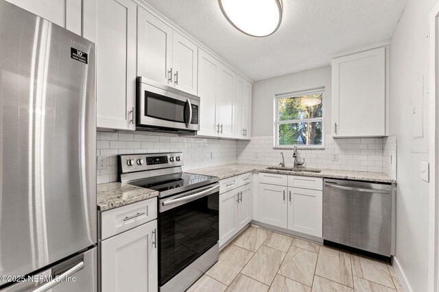 4651 Polaris St, Jacksonville, FL 32205 - kitchen featuring white cabinets, stainless steel appliances, a sink, light stone counters, and backsplash
