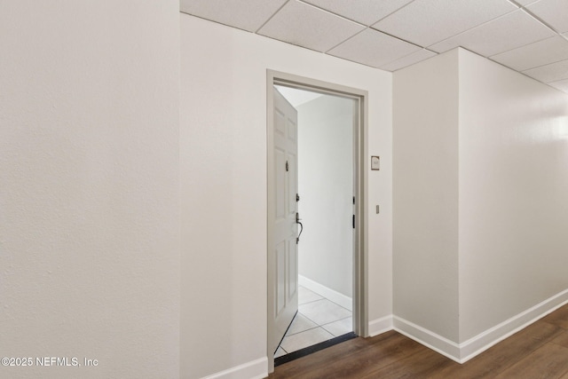hall featuring baseboards, wood finished floors, and a drop ceiling