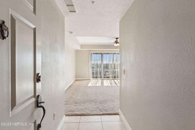hallway with a textured wall, a textured ceiling, visible vents, and light tile patterned floors