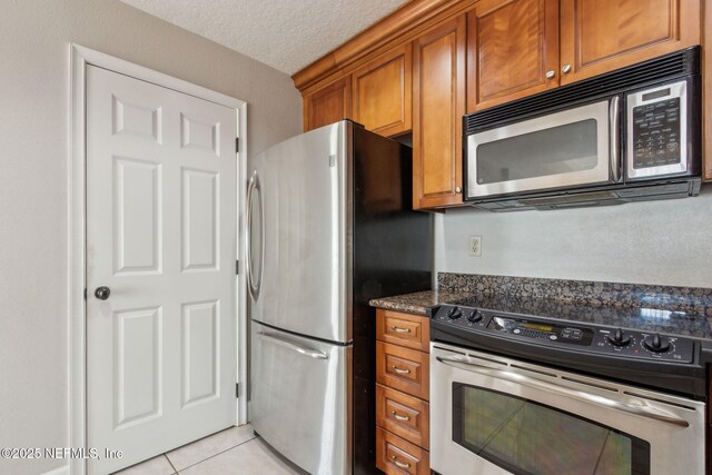 kitchen featuring light tile patterned floors, appliances with stainless steel finishes, a textured ceiling, and brown cabinets