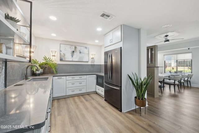 kitchen with a sink, freestanding refrigerator, black microwave, visible vents, and light wood-style floors