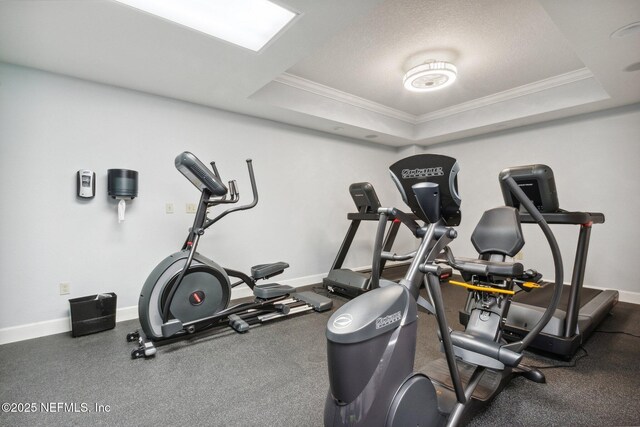 exercise area with baseboards, ornamental molding, and a raised ceiling