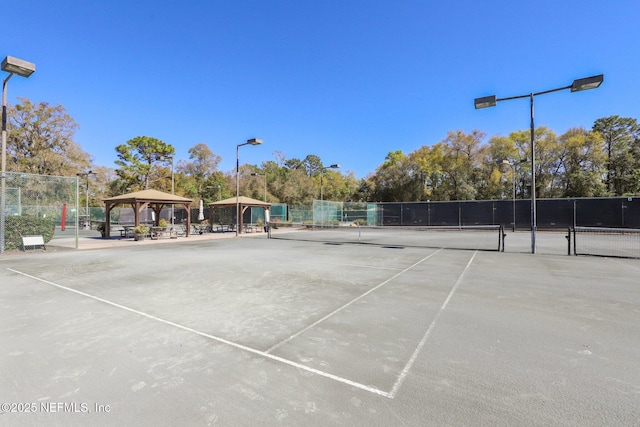 view of tennis court featuring fence and a gazebo