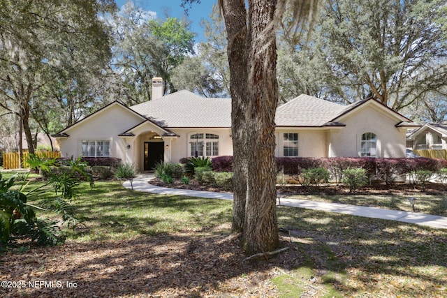 ranch-style house featuring a shingled roof, a chimney, stucco siding, and a front yard