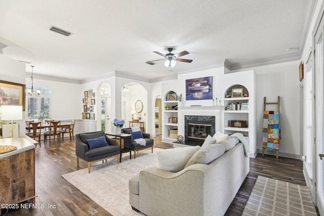living room with visible vents, a premium fireplace, arched walkways, dark wood-type flooring, and ceiling fan with notable chandelier
