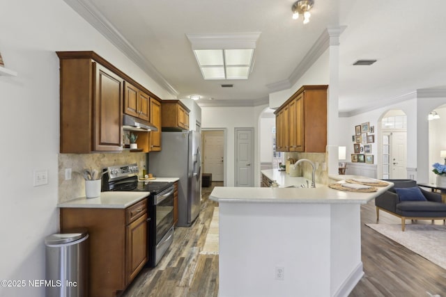 kitchen with crown molding, under cabinet range hood, arched walkways, a peninsula, and appliances with stainless steel finishes