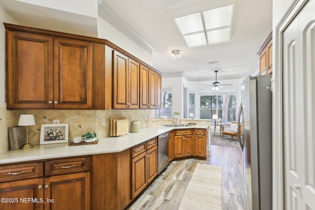 kitchen featuring a peninsula, stainless steel appliances, tasteful backsplash, a sink, and brown cabinetry