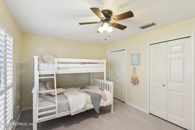 carpeted bedroom with baseboards, multiple closets, a textured ceiling, visible vents, and a ceiling fan
