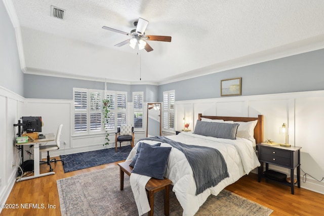 bedroom featuring visible vents, wood finished floors, a decorative wall, and a textured ceiling
