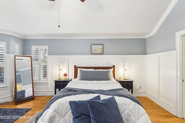 bedroom with wainscoting, crown molding, wood finished floors, and a decorative wall