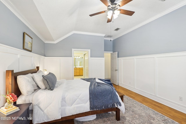 bedroom featuring lofted ceiling, wood finished floors, ensuite bath, and a wainscoted wall