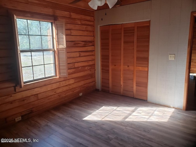 unfurnished bedroom with a closet, a ceiling fan, wood finished floors, and wooden walls