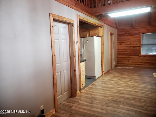 hallway featuring wooden walls, wood finished floors, and beam ceiling