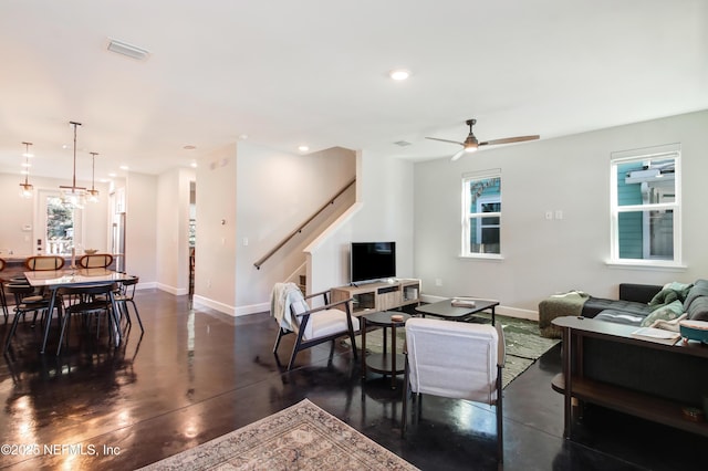 living area featuring ceiling fan, baseboards, finished concrete floors, and stairs