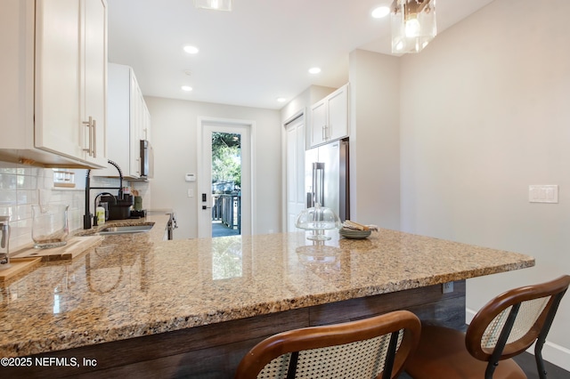 kitchen with decorative backsplash, a sink, high quality fridge, and light stone counters