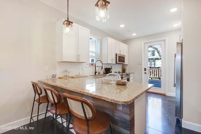 kitchen featuring a sink, white cabinetry, tasteful backsplash, appliances with stainless steel finishes, and a peninsula