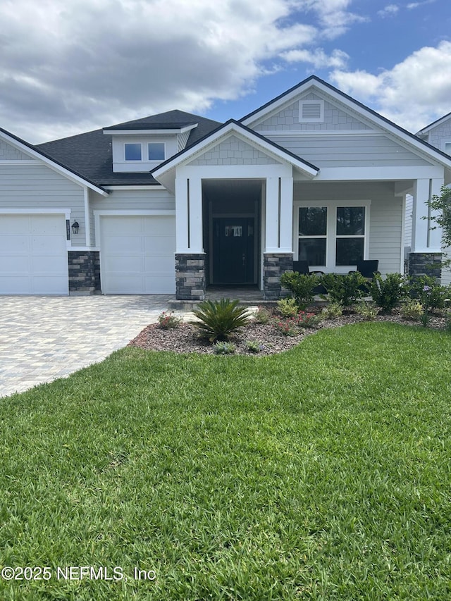 craftsman-style home featuring an attached garage, stone siding, a shingled roof, decorative driveway, and a front yard
