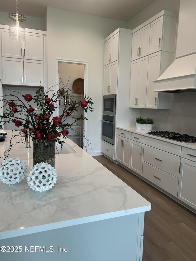kitchen with wall chimney exhaust hood, white cabinetry, dark wood-type flooring, and appliances with stainless steel finishes