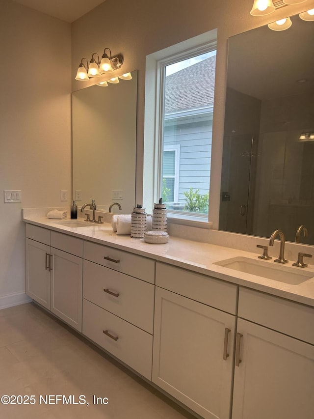 bathroom with a stall shower, baseboards, double vanity, and a sink