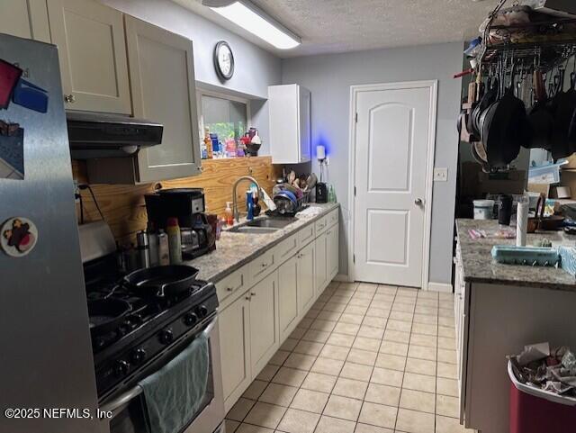 kitchen featuring a textured ceiling, a sink, light tile patterned floors, appliances with stainless steel finishes, and under cabinet range hood