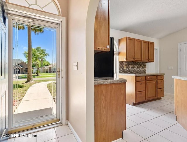 3387 Guernsey Ct, Jacksonville, FL 32226 - kitchen with backsplash, light tile patterned floors, arched walkways, freestanding refrigerator, and brown cabinetry