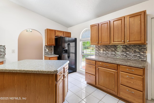 3387 Guernsey Ct, Jacksonville, FL 32226 - kitchen with black fridge, vaulted ceiling, backsplash, brown cabinetry, and a kitchen island