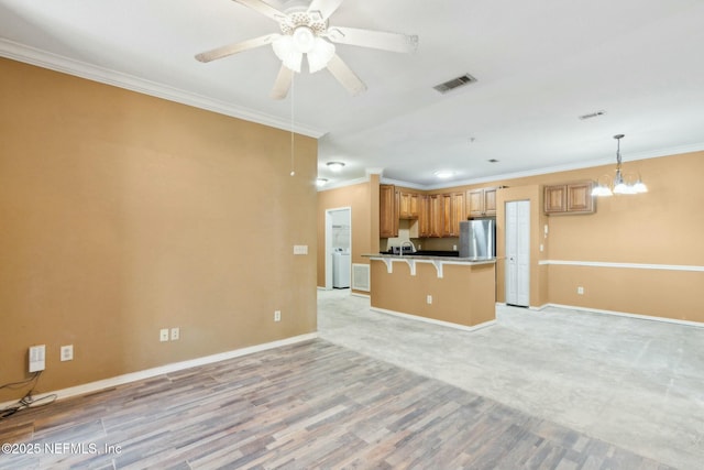 unfurnished living room featuring ceiling fan with notable chandelier, visible vents, baseboards, and ornamental molding