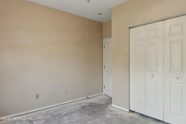 unfurnished bedroom featuring concrete floors, baseboards, and a closet