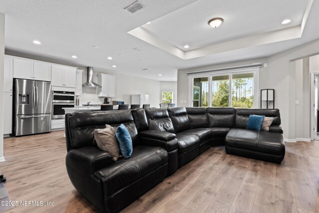 living area featuring a raised ceiling, light wood-style flooring, baseboards, visible vents, and recessed lighting
