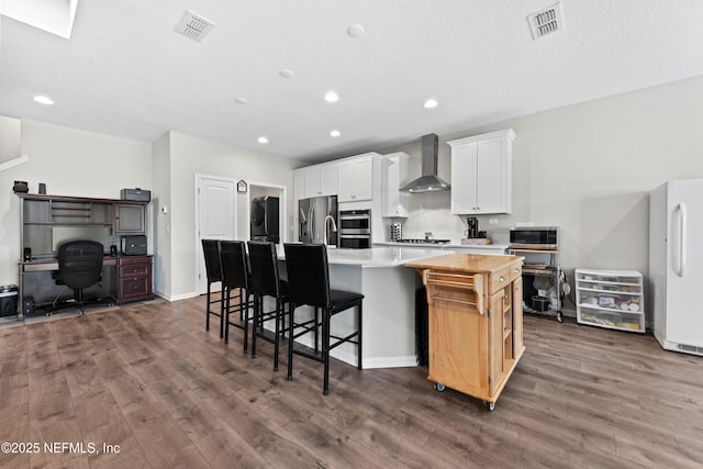 kitchen with light countertops, visible vents, stainless steel appliances, wall chimney exhaust hood, and a spacious island