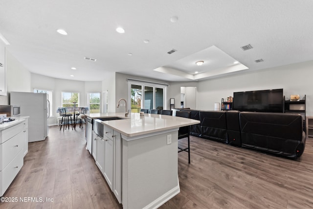 kitchen featuring light countertops, a breakfast bar, a sink, white cabinets, and wood finished floors