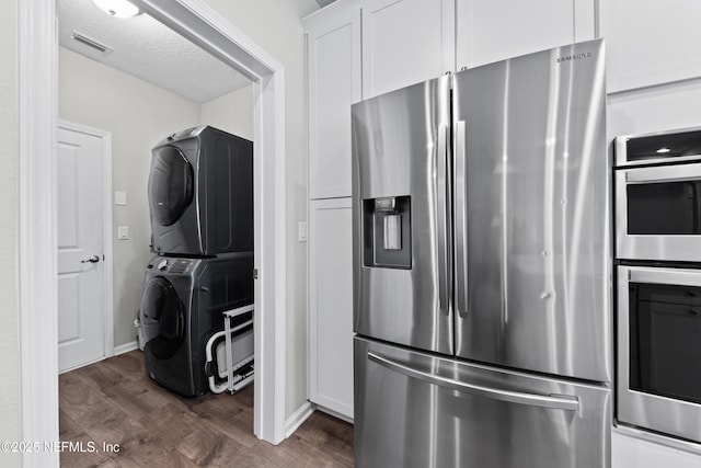 kitchen featuring white cabinetry, stacked washing maching and dryer, stainless steel fridge, visible vents, and dark wood-type flooring