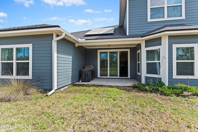 back of house featuring roof mounted solar panels, roof with shingles, a patio, and a lawn