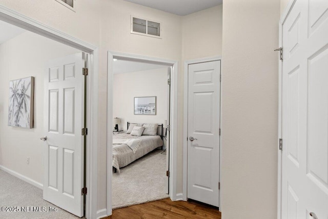 hallway featuring wood finished floors, carpet, baseboards, and visible vents