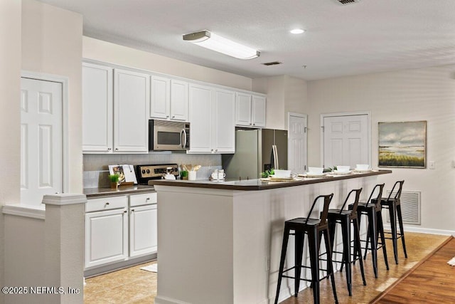 kitchen with white cabinets, an island with sink, stainless steel appliances, and dark countertops