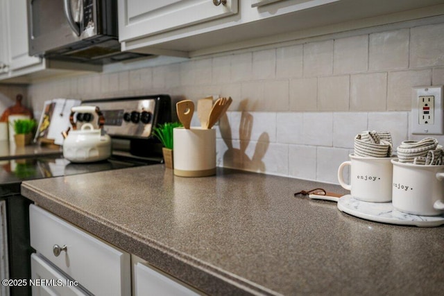 details featuring backsplash, white cabinets, dark countertops, and appliances with stainless steel finishes