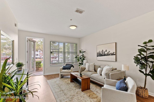living room featuring wood finished floors, a textured ceiling, baseboards, and visible vents