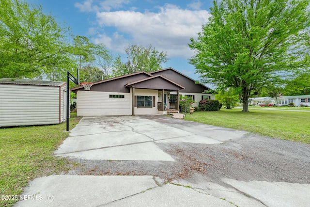 view of front of house featuring a shed, driveway, a front yard, and an outbuilding