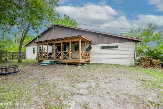 back of property featuring fence, a fire pit, and a deck