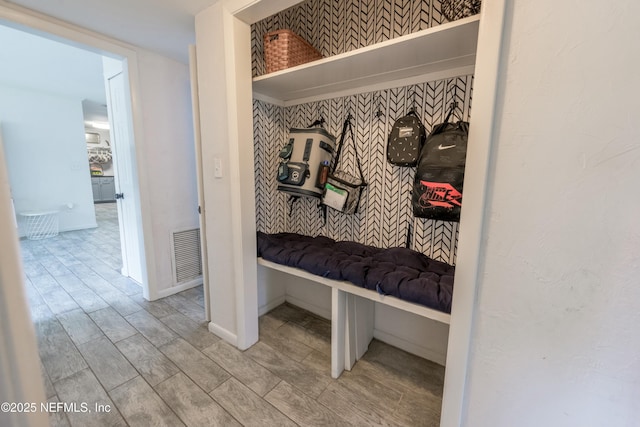mudroom with baseboards, an accent wall, wallpapered walls, visible vents, and wood finished floors