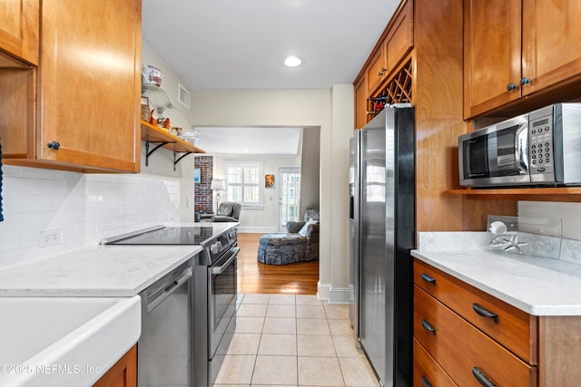 819 Lasalle St Unit 819, Jacksonville, FL 32207 - kitchen with light tile patterned flooring, decorative backsplash, stainless steel appliances, open floor plan, and brown cabinetry