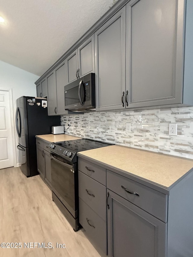 200 Nottingham Dr W, Saint Johns, FL 32259 - kitchen with black appliances, gray cabinetry, light wood finished floors, lofted ceiling, and decorative backsplash