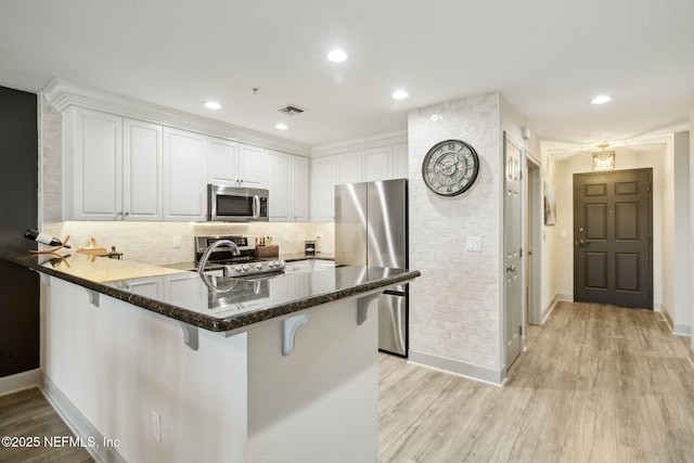 1478 Riverplace Blvd Unit 1103, Jacksonville, FL 32207 - kitchen featuring white cabinets, a peninsula, appliances with stainless steel finishes, light wood-type flooring, and a breakfast bar area