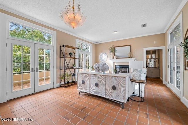 tiled living room with french doors, ornamental molding, a textured ceiling, visible vents, and a glass covered fireplace
