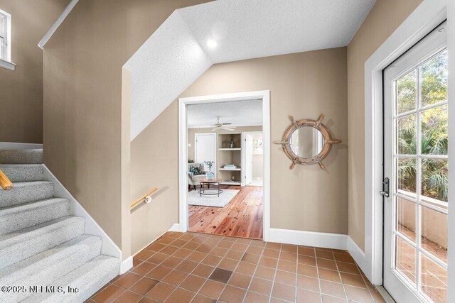 foyer featuring a textured ceiling, baseboards, ceiling fan, tile patterned floors, and stairway