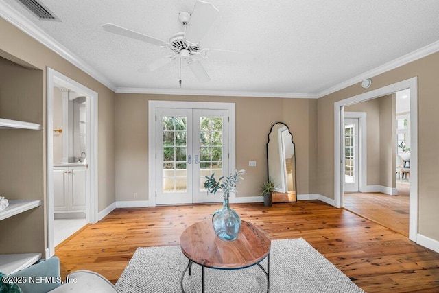 living area with crown molding, light wood-type flooring, french doors, a textured ceiling, and visible vents