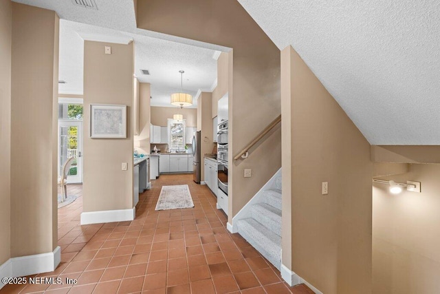 corridor featuring stairway, a textured ceiling, tile patterned flooring, baseboards, and visible vents