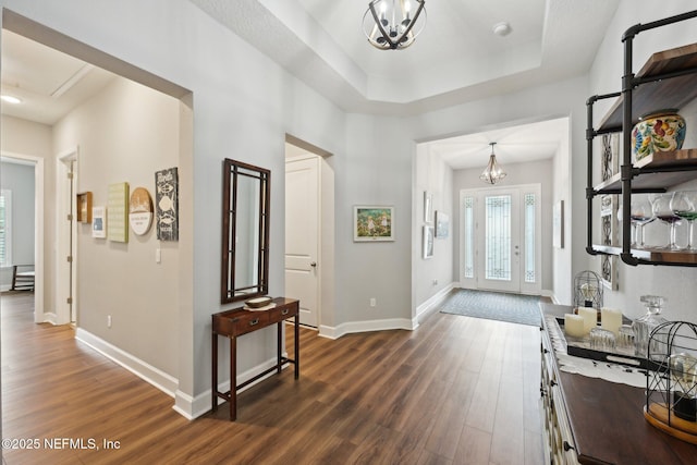 entrance foyer featuring a tray ceiling, baseboards, an inviting chandelier, and dark wood-style floors