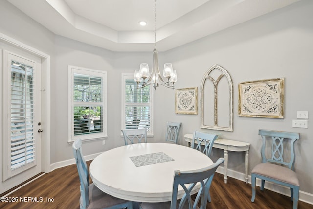 dining space with a chandelier, a raised ceiling, baseboards, and wood finished floors