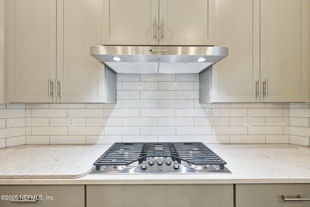 kitchen featuring under cabinet range hood, gray cabinetry, light stone countertops, decorative backsplash, and stainless steel gas cooktop